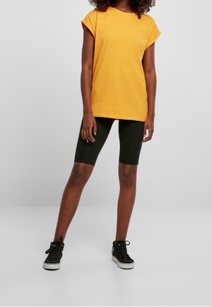 Gelbes, kurzärmliges Oversized-T-Shirt aus weichem Stoff, kombiniert mit schwarzen, knielangen Leggings und schwarzen High-Top-Sneakers.