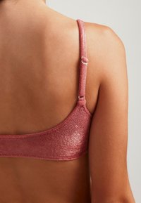 Sostén de color rosa con tejido texturizado, tirantes ajustables y un respaldo suave y redondeado. Presenta un diseño simple sin adornos.