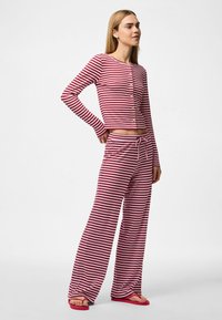 Sarkans un balts svītrots atpūtas komplekts, kurā ietilpst pogājams garām piedurknēm tops un brīva piegriezuma bikses ar savelkamu jostasvietu. Tekstūra audums.