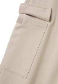 Beiger Baumwollstoff mit einer großen Seitentasche, die mit einem Klettverschluss geschlossen wird, und genähten Kanten für Langlebigkeit. Glatte Textur mit dezenten Details.
