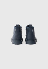 Stivaletti alla caviglia in pelle blu navy con superficie testurizzata, caratterizzati da un accento blu sul colletto, chiusura con zip e suole spesse e tassellate.