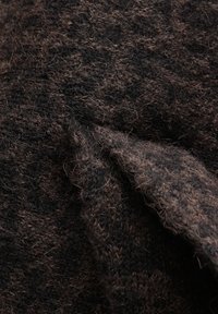 Tessuto di lana testurizzato in marrone scuro e nero, caratterizzato da un aspetto morbido e peloso e una trama irregolare, che mostra pieghe stratificate e profondità.