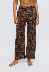 Pantalon de pyjama imprimé léopard en marron et noir, avec une coupe large et une taille élastique. Le tissu semble doux avec une texture lisse.