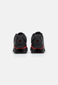 Schwarze Sportschuhe mit einer strukturierten Oberfläche, roten Akzenten und einem auffälligen, von hinten sichtbaren, gepolsterten Sohlen-Design.