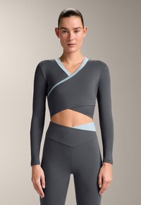 Top corto grigio a maniche lunghe con design incrociato e accenti azzurri, abbinato a leggings a vita alta, texture liscia.