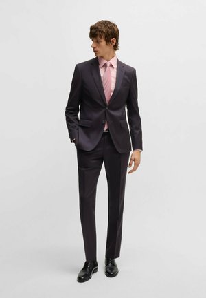 Donker op maat gemaakt kostuum met een getailleerd silhouet, gecombineerd met een lichtroze overhemd en stropdas. Glad materiaal, zakken op het jasje en de broek, zwarte schoenen.