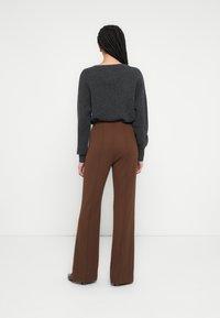 Sivý pletený sveter s uvoľneným strihom a širokým okrúhlym výstrihom, skombinovaný s hnedými, vysokým pásom a rozšírenými nohavicami. Hladká textúra látky.