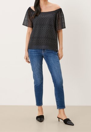 Haut noir épaules dénudées avec manches transparentes brodées, associé à un jean skinny bleu et des mules noires à bouts pointus.