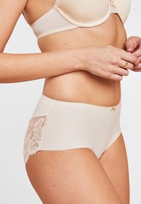 Beige ondergoed met een gladde voorkant en bloemenkantdetail aan de zijkant, met een klein strikaccent op de tailleband.
