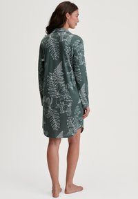 Abito a maniche lunghe in tessuto verde scuro con motivi floreali e felci bianchi. Il design include un colletto e spacchi laterali all'orlo.