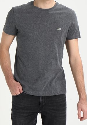 T-shirt in cotone grigio con scollo a girocollo e maniche corte, caratterizzato da un piccolo logo di coccodrillo verde sul petto sinistro. Vestibilità casual.