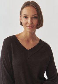 Musthave musta V-kaelusega sviiter tekstureeritud viimistlusega ja avarate varrukatega; omab lõdva lõiget. Kangas näeb välja pehme ja sellel on õrn sära.