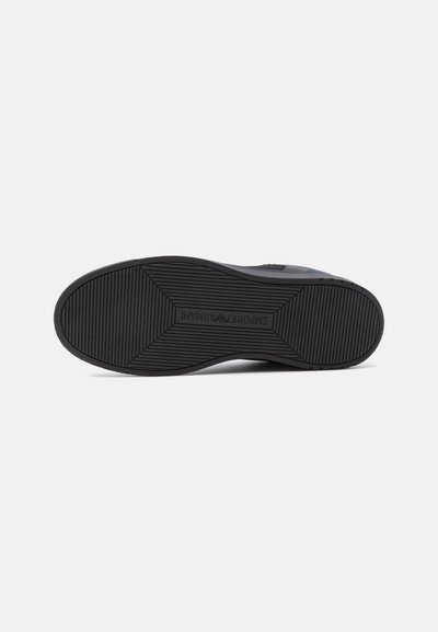 Semelle de chaussure noire avec des rainures horizontales et le logo Emporio Armani embossé au centre sur un fond blanc uni.