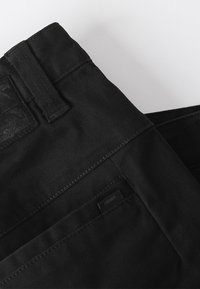 Μαύρα τζιν από ντένιμ με υφή, διακριτές ραφές, δερμάτινη ετικέτα στη μέση και μια μικρή ετικέτα από ύφασμα στην τσέπη.