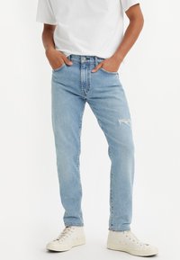 Ljusblå denimjeans med lös passform, med detaljerad slitning vid knäna och klassisk femficksdesign. Matchat med vita sneakers.