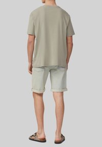 T-shirt en coton vert clair, à manches courtes, coupe décontractée, associé à un short en denim clair avec les bords retroussés et des sandales marron à lanières.