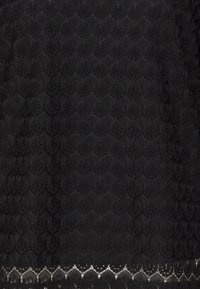 Tissu en dentelle noire avec un motif géométrique, présentant une surface texturée et un délicat bord festonné en bas.