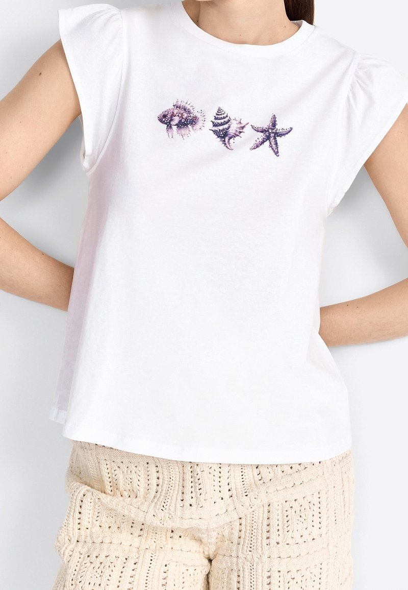 Camiseta blanca de manga corta con mangas abullonadas, que presenta gráficos de conchas moradas y estrellas de mar en la parte delantera. La tela parece suave y lisa.