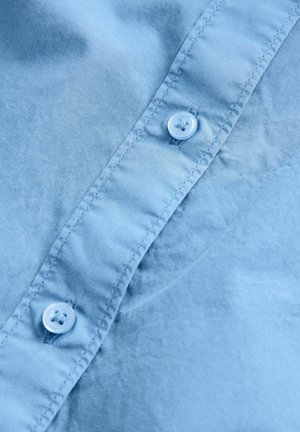 Himmelblaues Baumwollhemd mit glatter Textur, Knopfverschluss und zwei Knöpfen mit kreisförmigen, hellblauen Verzierungen.