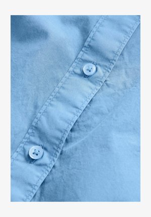 Lichtblauw stoffen overhemd met een gladde textuur, een knoopsluiting en twee knopen met ronde, lichtblauwe versieringen.