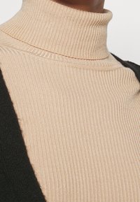 Beżowy, prążkowany golf o dopasowanym kroju, zestawiony z czarną dzianinową nakładką. Teksturowana tkanina o miękkim wyglądzie.