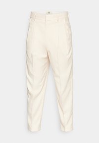 Beżowe spodni z dopasowanym krojem, charakteryzujące się gładką teksturą, szlufkami na pasek i fałdami z przodu. Tkanina wydaje się lekka.