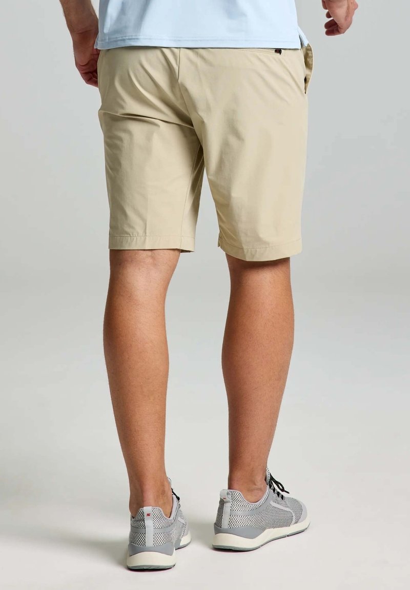 Shorts beige avec une coupe décontractée, fabriqués en matériau léger. Détails avec des poches latérales et associés à des baskets en mesh gris.