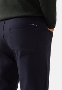 Pantalones azul marino de tela lisa, con un bolsillo trasero con costuras sutiles y un pequeño logotipo impreso encima.