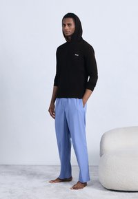 Mustast kapuutsiga pika varrukaga dressipluus rinnal oleva logoga, kombineeritud helesiniste pükstega. Mõlemad rõivad on lõdva istuvusega.