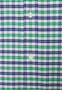 Vit tyg med grön och blå rutmönster, med två vita knappar sydda i den centrala vertikala sömmen.