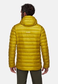 Veste isolée jaune avec une capuche, présentant un design matelassé, une texture lisse et un petit logo de marque au dos.