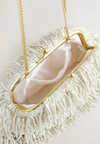 Bílá korálková kabelka se zlatým kovovým rámečkem, s řetízkovým popruhem a saténovou vnitřní podšívkou. Korálky vytvářejí texturovaný detail třásní.