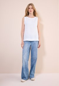 Weißes, ärmelloses Leinenoberteil kombiniert mit hellblauen, weit geschnittenen Jeans. Das Oberteil hat einen runden Ausschnitt, gesäumte Kanten und eine glatte Textur.