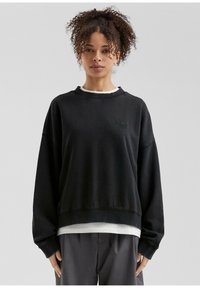 Felpa nera oversize con scollatura rotonda, polsini a coste e un logo discreto. Presenta una texture morbida e una vestibilità comoda.