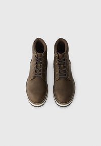 Brown leather boots featuring a high-top design, lace-up front, contrasting cream stitching, and a textured rubber sole.
