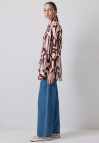 Langærmet, button-up skjorte i creme med burgundy abstrakte mønstre. Bæres med brede blå denim jeans og hvide sneakers.