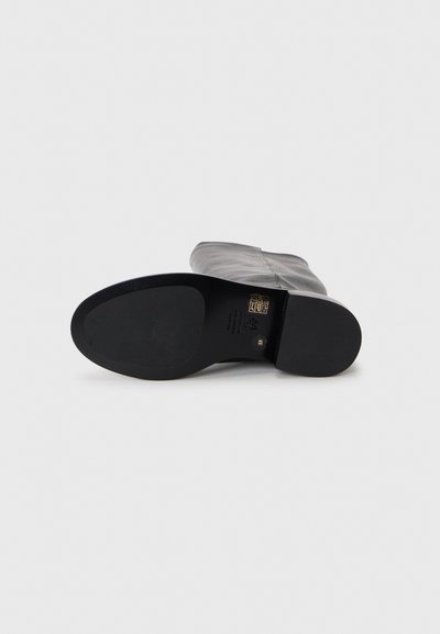 Stivale alla caviglia in pelle nera con texture liscia, punta arrotondata e suola piatta in gomma. Presenta una cucitura sottile lungo il lato.