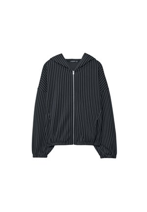 Črna jakna z zadrgo, z navpičnimi belimi črtami, z ruto in elastičnimi manšetami; ima kratko zasnovo in gladko teksturo tkanine.