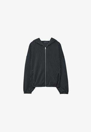 Črna jakna z zadrgo, z navpičnimi belimi črtami, z ruto in elastičnimi manšetami; ima kratko zasnovo in gladko teksturo tkanine.