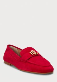 Mocassin en daim rouge avec un bout arrondi, un emblème doré "RL" bien en vue sur la sangle et une semelle plate marron. Texture lisse.