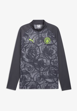 Camiseta deportiva de manga larga de color gris oscuro del Manchester City con patrón repetido del escudo del club, logo de Puma en amarillo neón y cuello con cremallera hasta un cuarto.