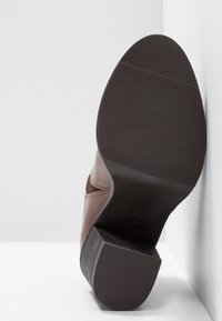 Stivale alla caviglia in pelle marrone con suola in gomma nera testurizzata. Il tacco è spesso e lo stivale presenta dettagli di cucitura sottili.