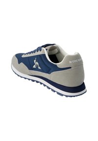 Zapatilla azul marino con parte superior de ante y sintético, cordones blancos, acentos grises y suela de goma con un patrón texturizado.