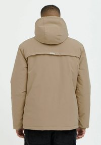 Beige hooded jacket with a smooth, matte finish. Features a back panel design and a small label near the shoulder. Full-zip closure and side pockets.