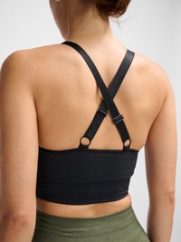 Femme portant un soutien-gorge de sport noir avec des bretelles croisées réglables et des leggings taille haute vert olive, vue de dos.