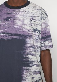Tričko s krátkým rukávem s abstraktním potiskem v purpurové, bílé a navy modré. Vyrobeno z m ěkké látky, s kulatým výstřihem a volným střihem.