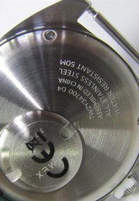 Achterkant van een roestvrijstalen polshorloge met gegraveerde tekst die waterbestendigheid, assemblageplaats, modelnummer en certificeringsmerken toont.