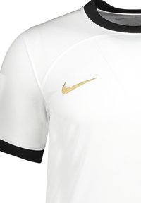 Maillot de sport Nike blanc avec des accents noirs sur le col et les manches, présentant un logo Nike doré à l'avant. Tissu lisse et respirant.