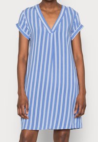 Blå randig klänning med djup V-ringning och rullade korta ärmar. Har vita vertikala ränder och en lös, avslappnad passform.