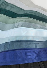 Stivă de benzi elastice pentru lenjerie împăturită în diverse nuanțe de albastru și verde, fiecare având logo-ul "NEXT" țesut în material.